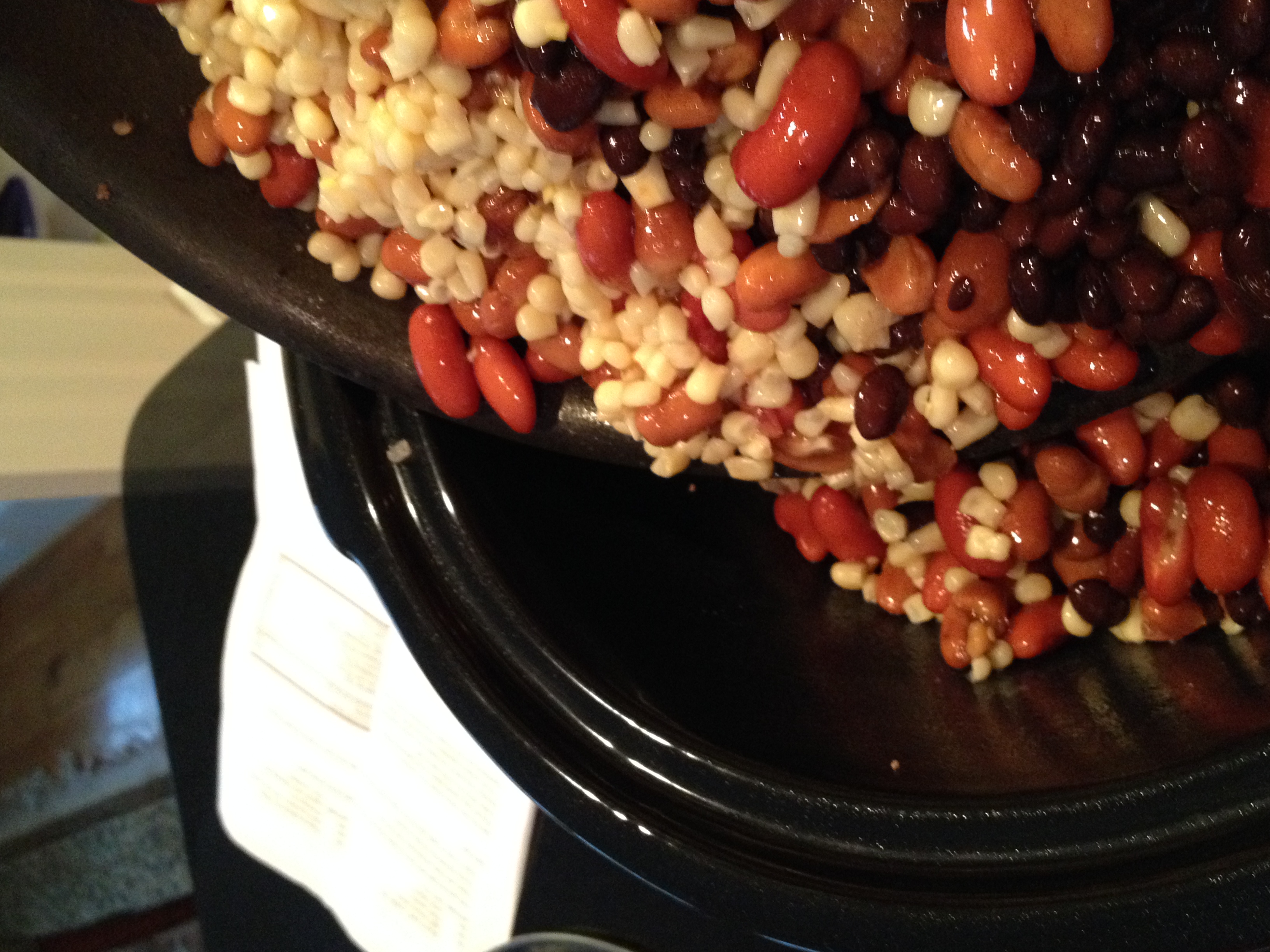 Using skillet to pour beans and corn into crock pot on top of cooked ground beef and onions.